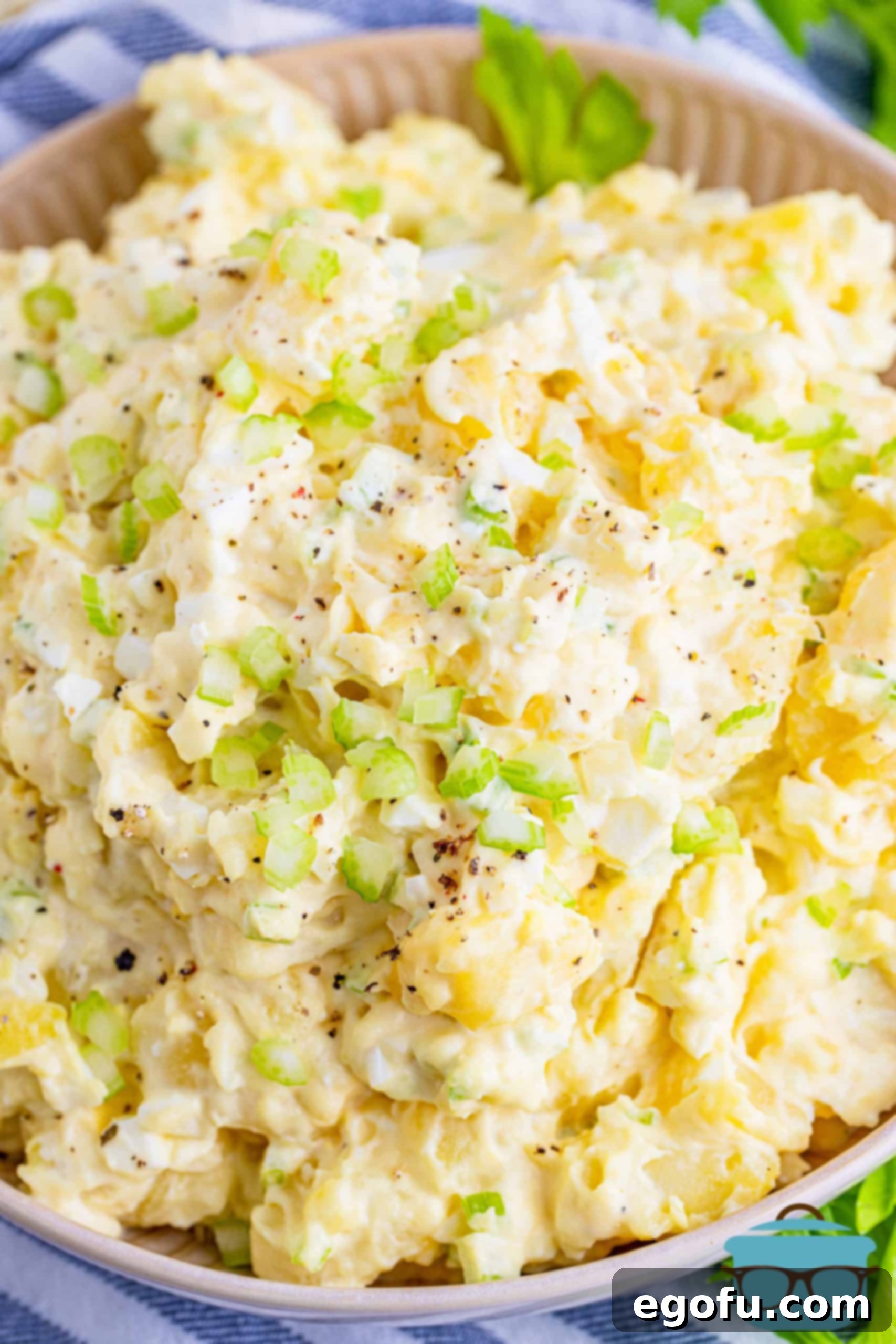 Closeup photo of a generous serving of the best creamy potato salad in a decorative bowl, highlighting its rich texture and appealing ingredients.