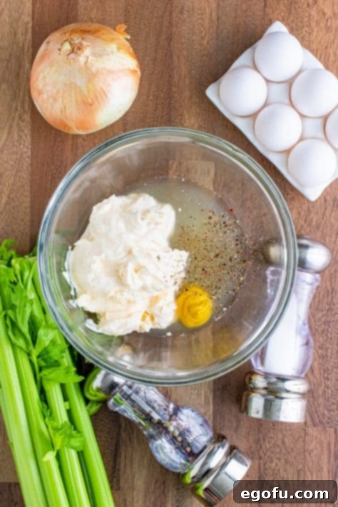 A clear mixing bowl showcasing the creamy dressing ingredients: mayonnaise, yellow mustard, chicken stock, salt, and pepper, all blended smoothly.