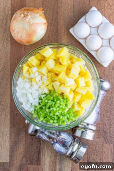 Cooked diced potatoes, finely chopped celery, and diced onion being gently folded into the creamy dressing mixture in a large clear bowl.