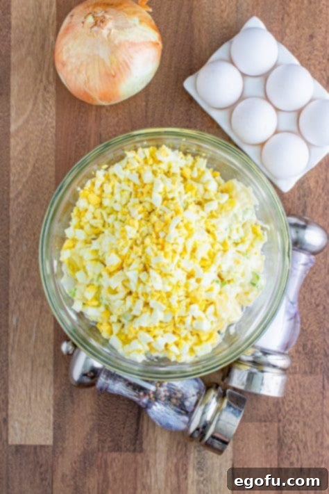 Roughly chopped hard-boiled eggs being carefully added and gently folded into the potato salad mixture in a large bowl.