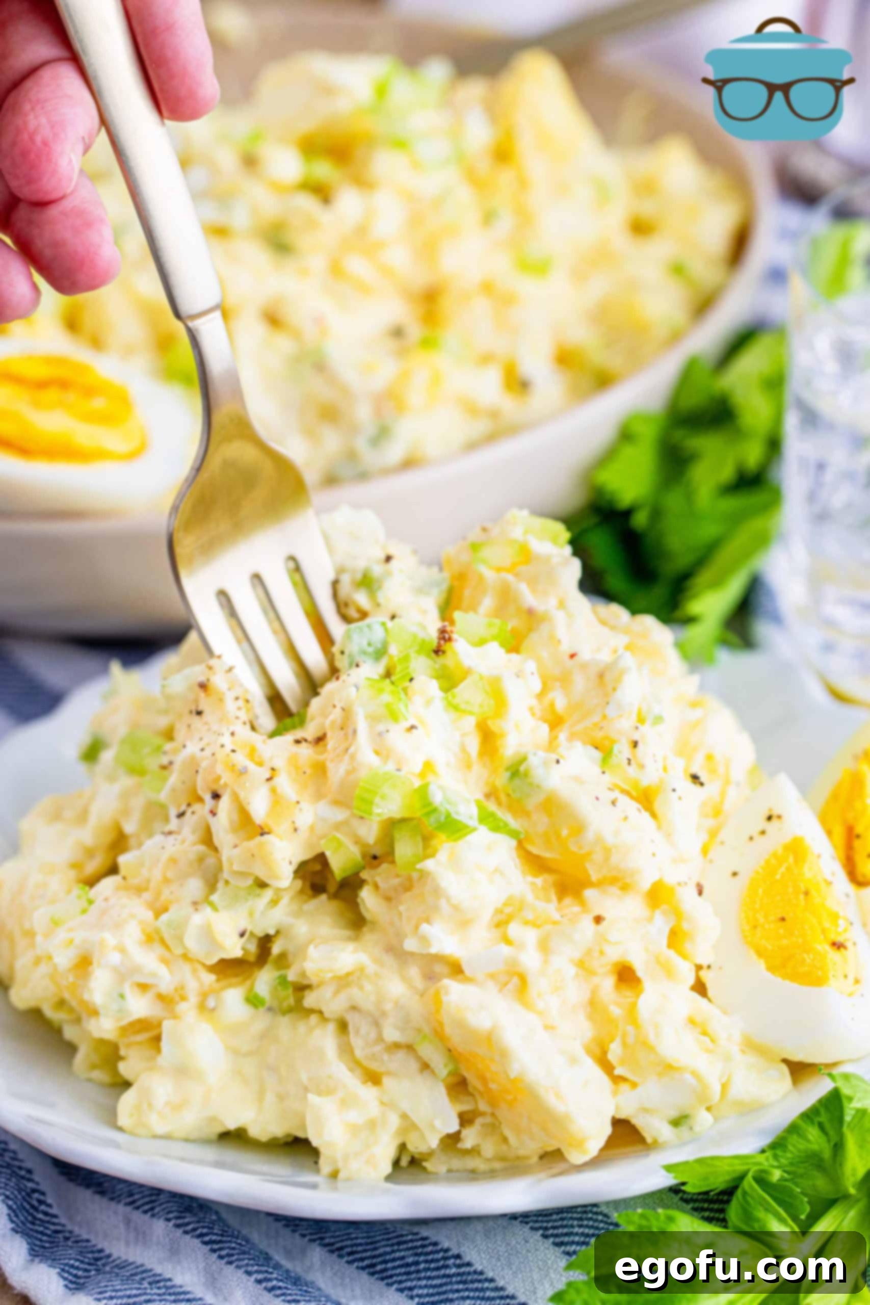 A single serving of the creamy potato salad beautifully presented on a small white plate with a fork inserted, ready to be eaten.