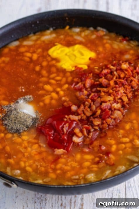 Hearty Comfort Baked Beans 12 A skillet with beans, onions, bacon, salt, pepper, mustard, ketchup, maple syrup, and molasses.