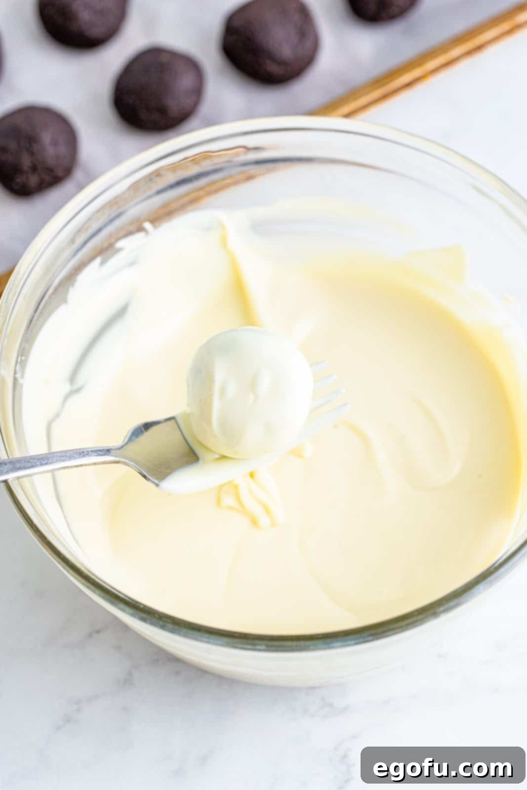 a spoon removing chocolate covered oreo cookie ball from bowl.