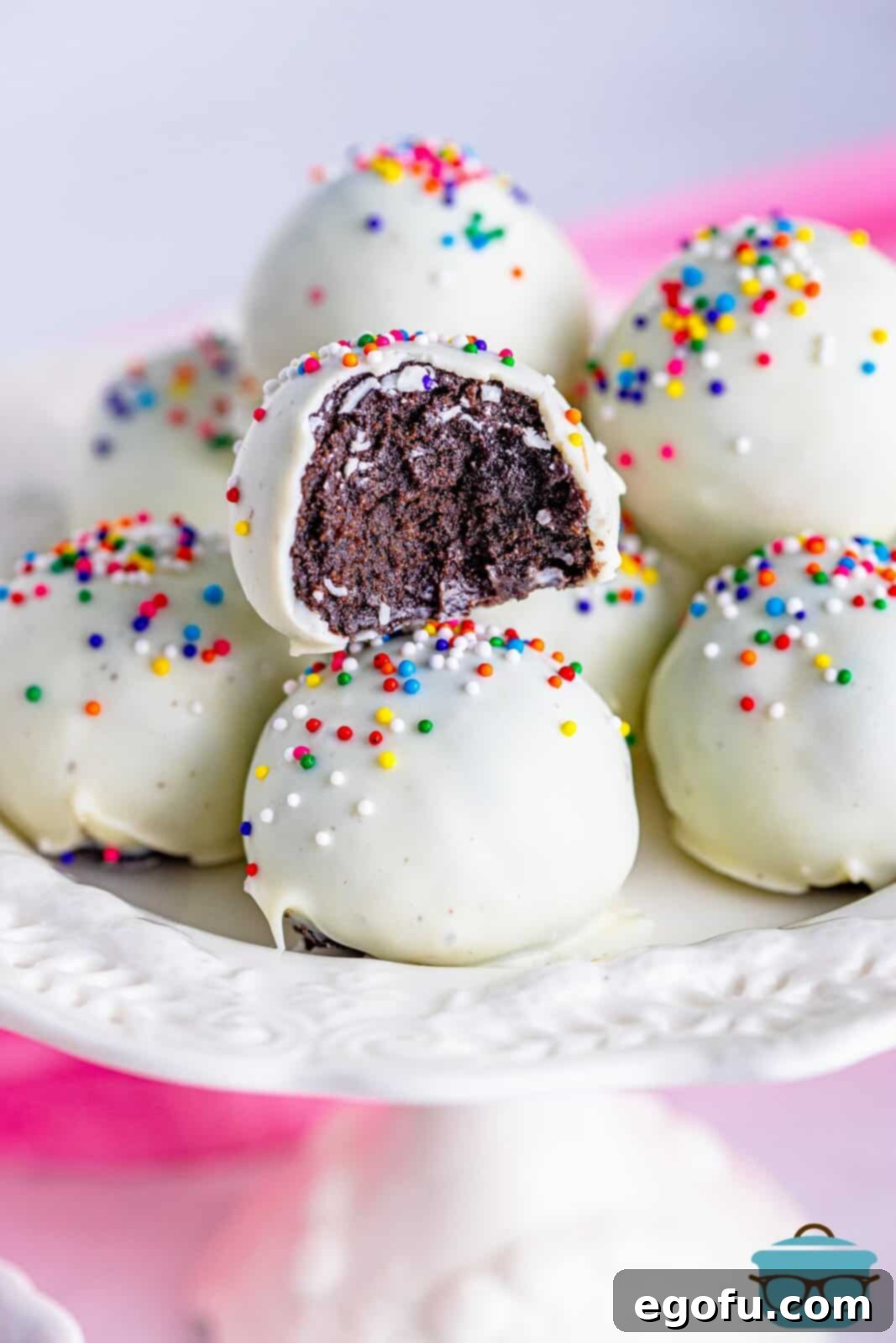 cookie balls on a white cake pedestal stand with one cookie ball showing a bite removed.