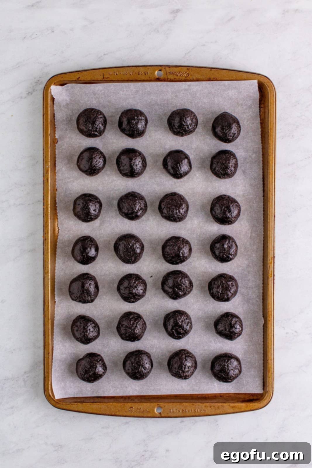 cookie balls shown on parchment paper on a cookie sheet.