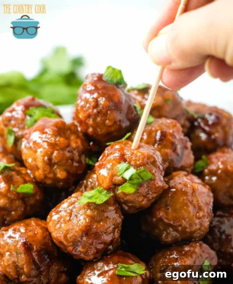 a hand pushing a toothpick into a meatball that is at the top of a pile of other meatballs.