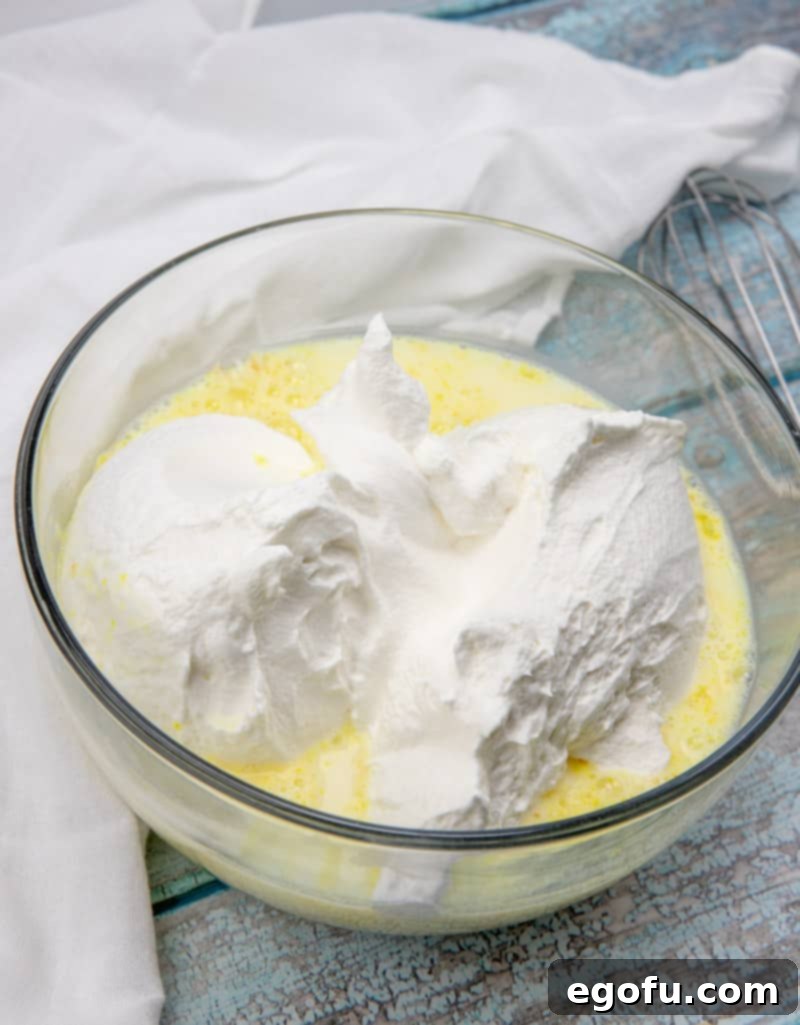 Milk, instant vanilla pudding mix, and cool whip being mixed together in a large glass bowl to create the creamy filling.
