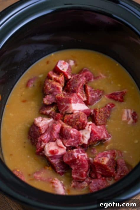Beef being added to a Crockpot with broth in it.