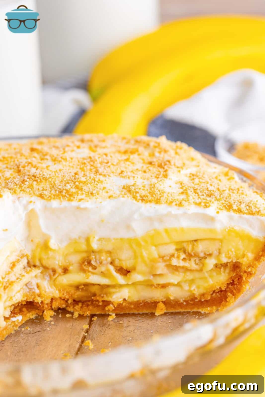 Golden Banana Dream Pie 2 A beautifully presented banana pudding pie with a slice removed, revealing its inviting layers of Nilla wafer crust, fresh banana slices, and creamy pudding. Topped with fluffy whipped cream and a sprinkle of crumbs.