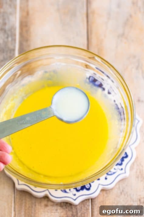 Golden Banana Dream Pie 20 A small amount of warm milk being carefully added to lightly beaten egg yolks in a bowl, tempering them.