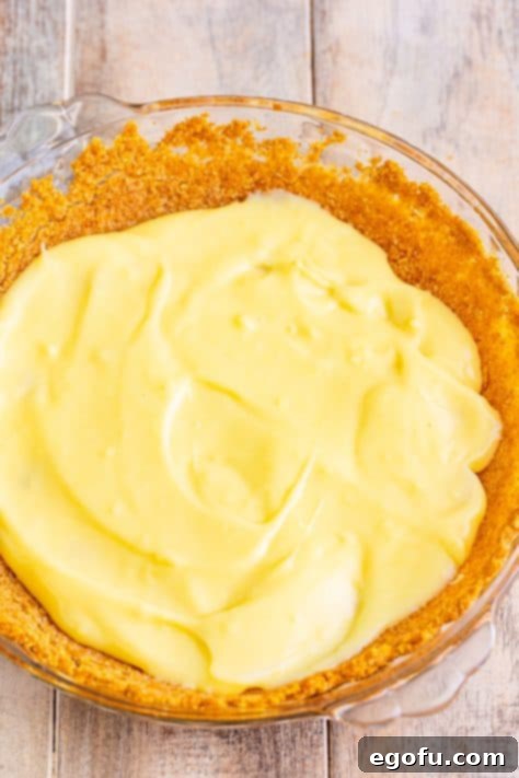 Golden Banana Dream Pie 23 Creamy homemade banana pudding being spread over the first layer of sliced bananas in the pie crust.