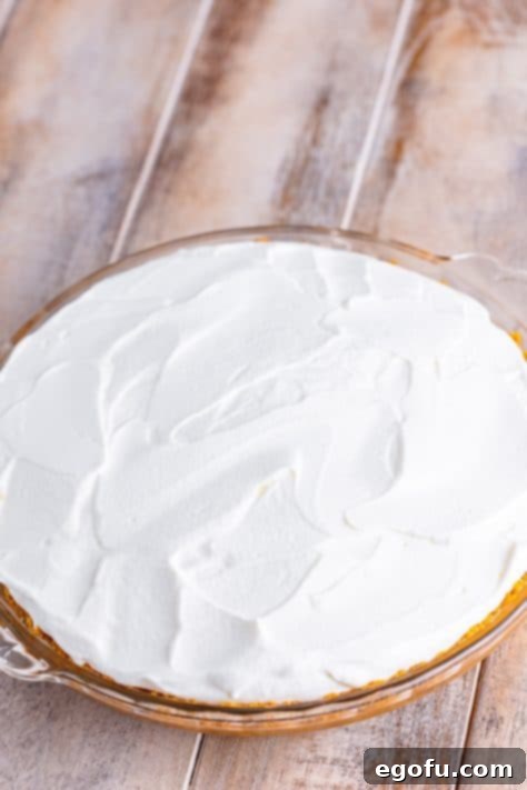 Golden Banana Dream Pie 28 Fluffy whipped cream being carefully spread over the top of the chilled banana pudding pie.