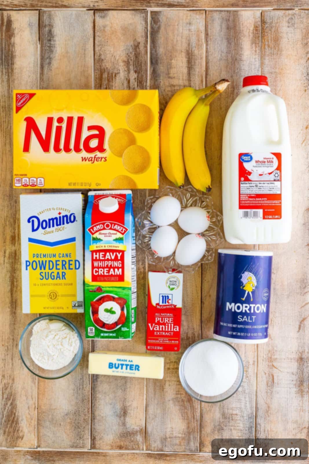 Golden Banana Dream Pie 4 A vibrant flat lay showcasing all the essential ingredients for Banana Pudding Pie: Nilla wafers, ripe bananas, whole milk, eggs, heavy cream, powdered sugar, vanilla extract, salt, granulated sugar, butter, and flour.