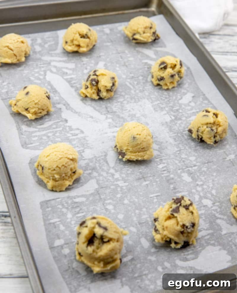 Neatly rolled chocolate chip cookie dough balls arranged on a baking tray lined with parchment paper, spaced apart for optimal baking.