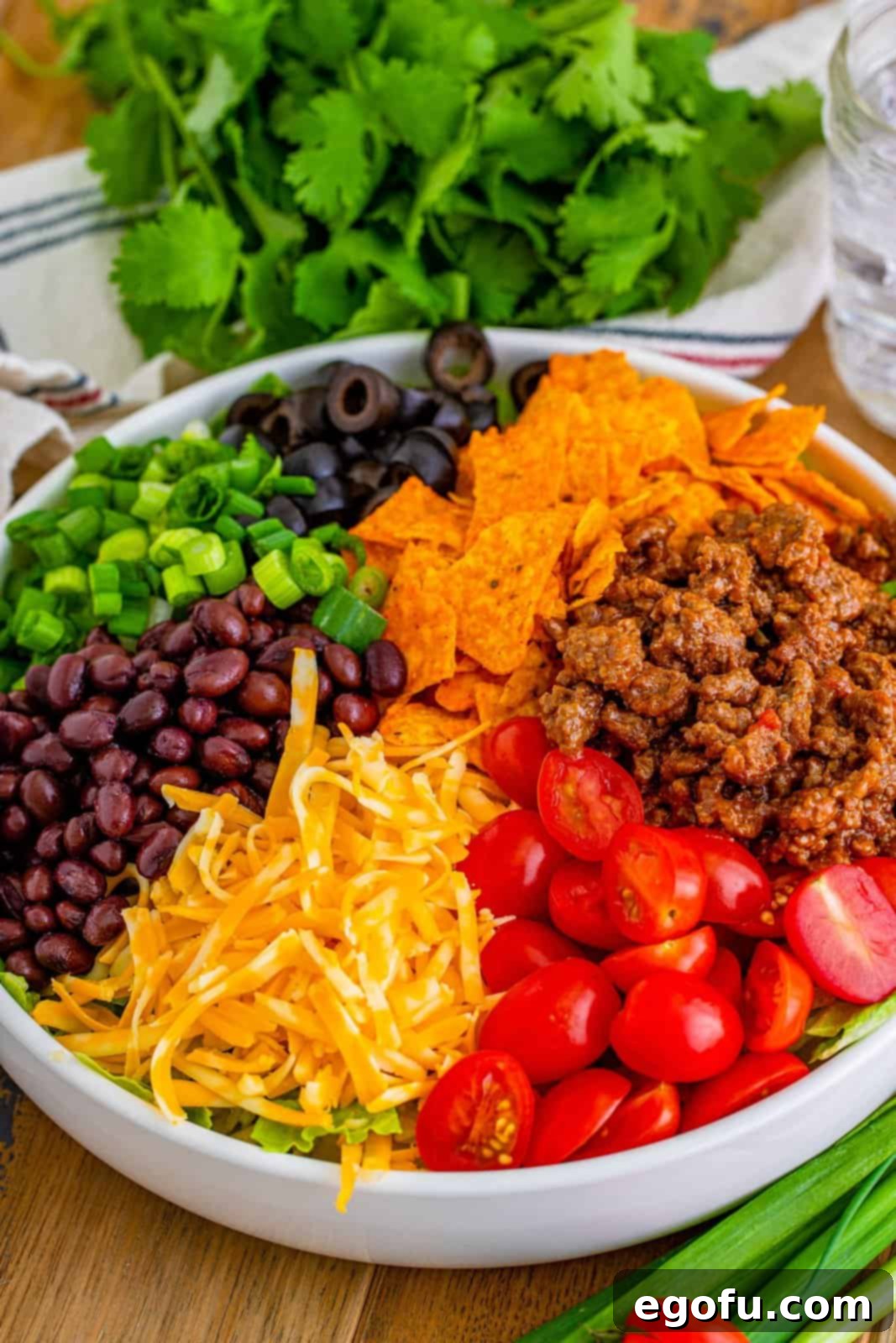 Doritos Fiesta Salad 7 Various Doritos Taco Salad ingredients, including seasoned beef, beans, lettuce, cheese, and tomatoes, arranged in a large mixing bowl before stirring.