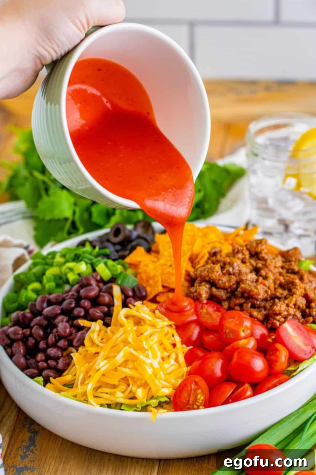 Doritos Fiesta Salad 8 Catalina dressing being drizzled over a large bowl of Doritos Taco Salad ingredients.