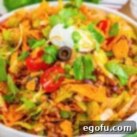 Doritos Fiesta Salad 10 A close-up of Doritos Taco Salad in a bowl, showing the colorful mix of ingredients and a creamy dressing drizzle.