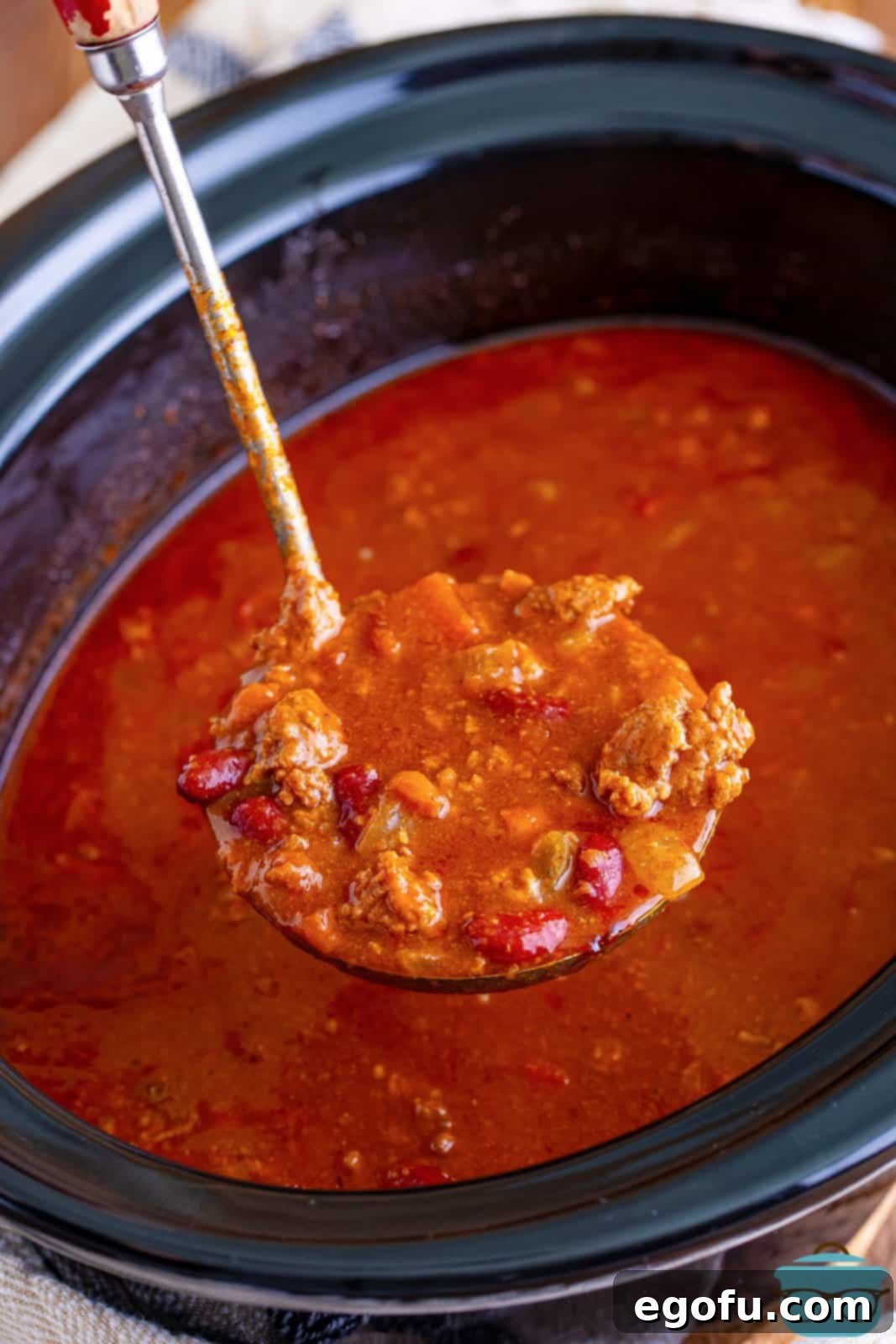 a ladle holding up a serving of chili over the slow cooker. 