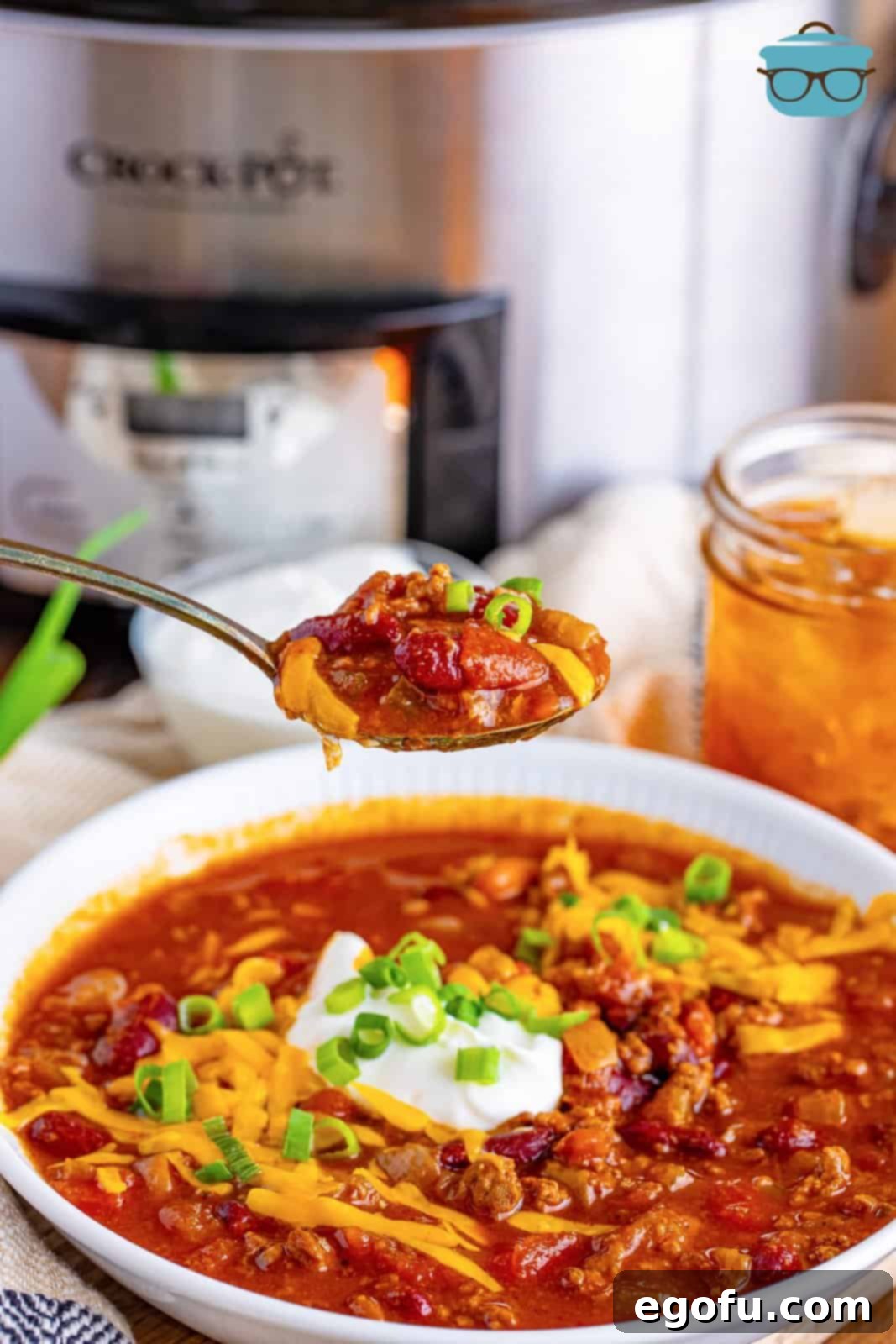 a spoon holding up some chili over a bowl. 