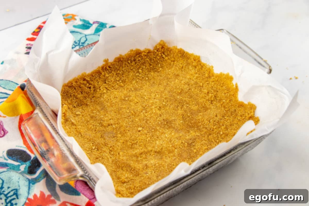 The delicious graham cracker crust mixture pressed firmly and evenly into a square baking pan, ready for its first bake.