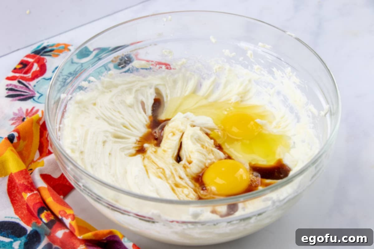 A bowl filled with softened cream cheese, eggs, and vanilla extract, perfectly mixed together into a smooth, creamy cheesecake batter.
