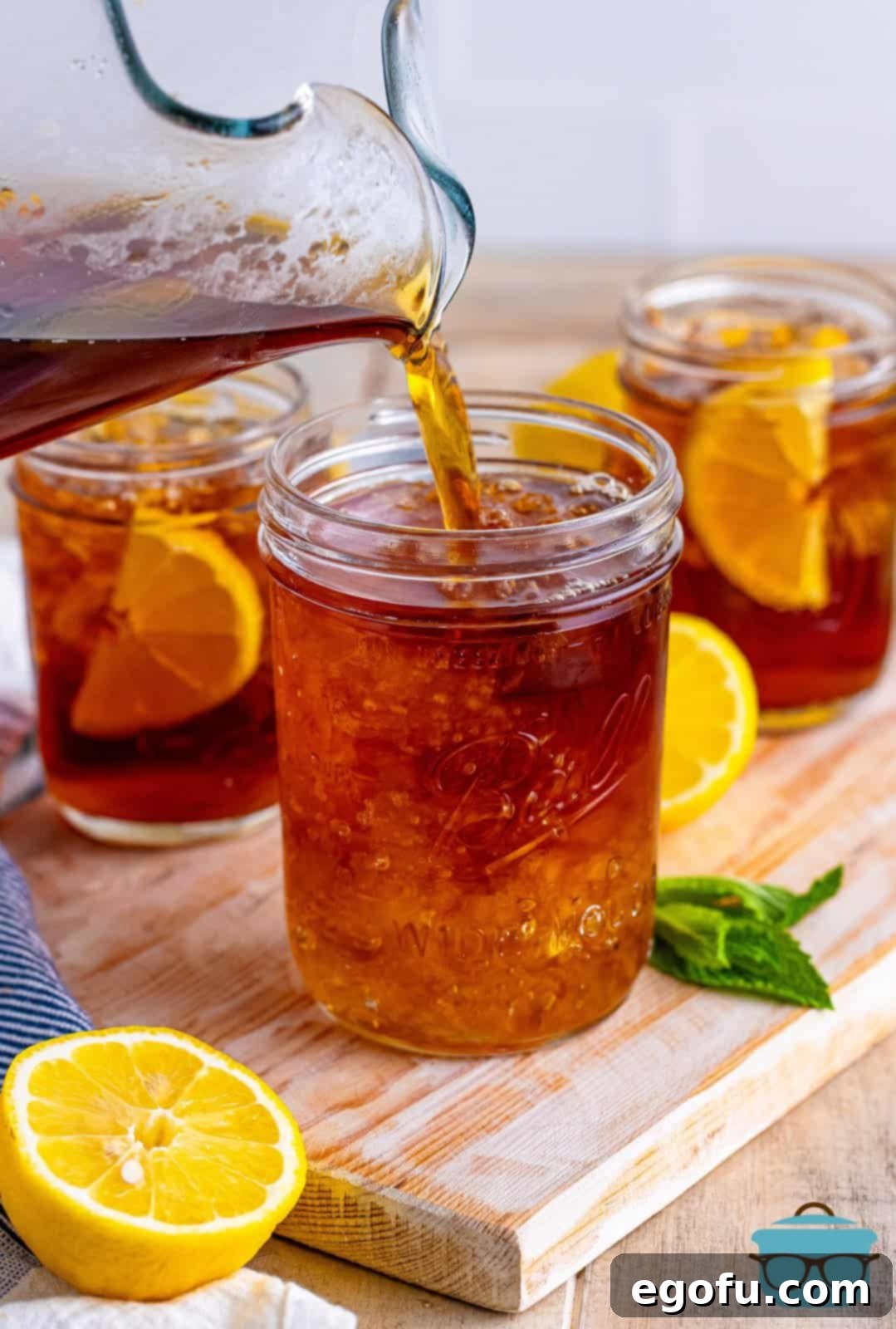 A pitcher of iced tea being poured into a small mason jar filled with crushed ice, ready for serving.