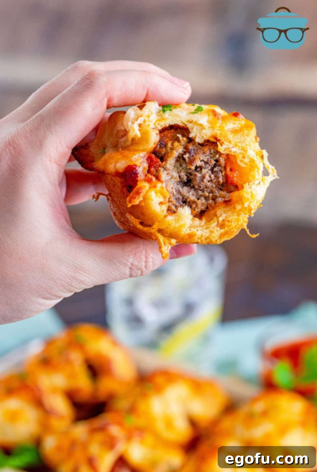 Hand holding up one Meatball Sub Cup with bite taken out showing inside.