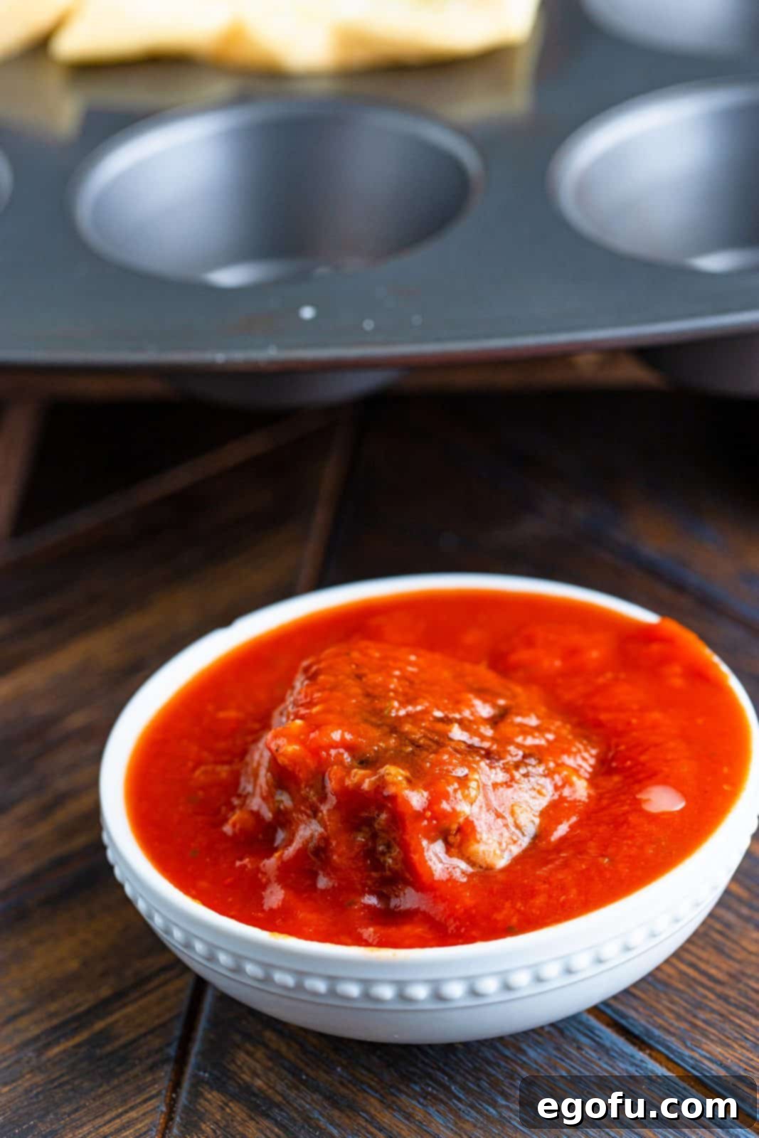 Meatball in bowl of marinara sauce covering it.