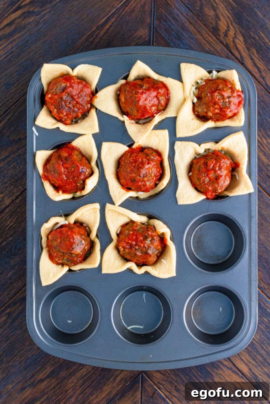 Meatballs added to top of cheese in muffin tin.