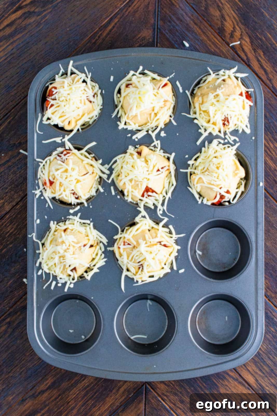 Cheese placed on top of folded crescent dough sheets in muffin tin.