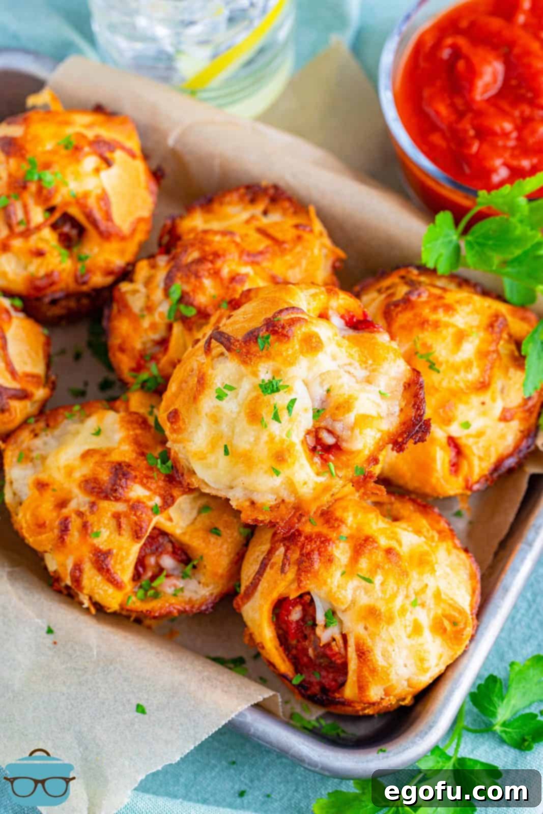 Overhead of Meatball Sub Cups stacked on parchment lined pan.