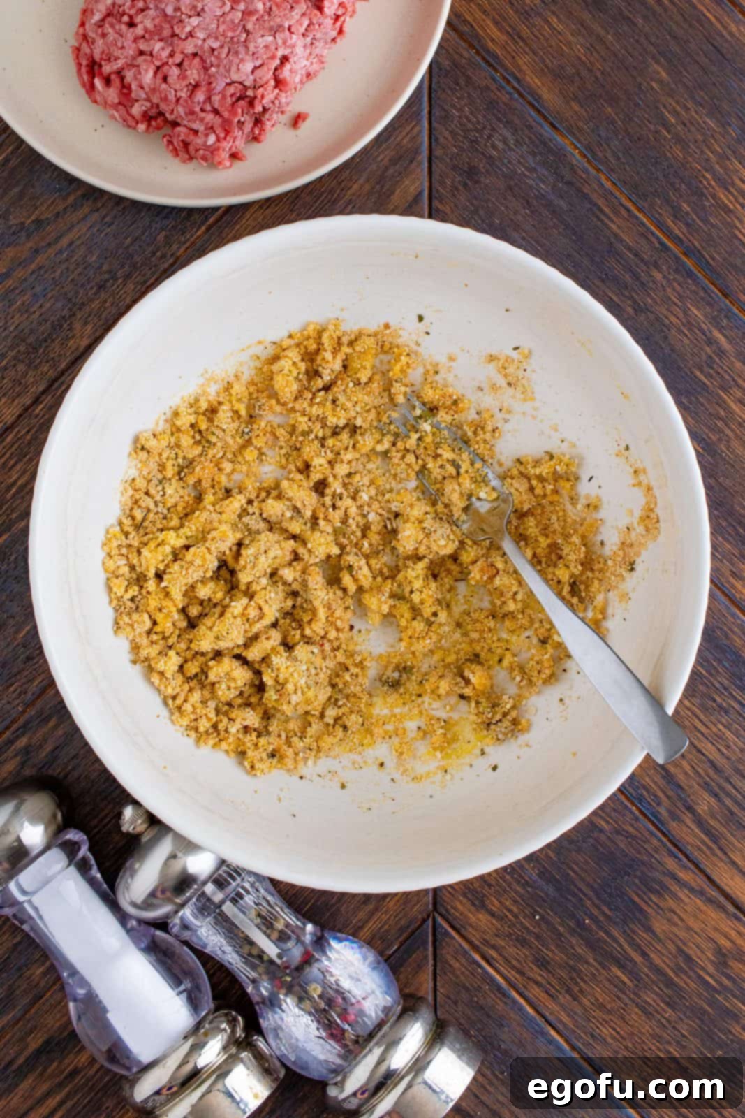 Egg, parmesan, breadcrumbs, garlic powder, onion powder, oregano, salt, and pepper mixed together in white bowl.