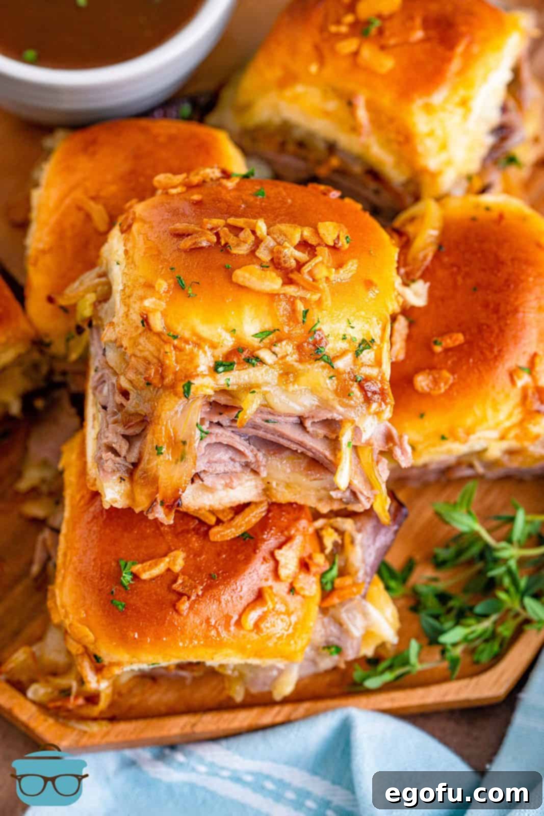 Stacked French Dip Sliders on wooden plate showing melted cheese.