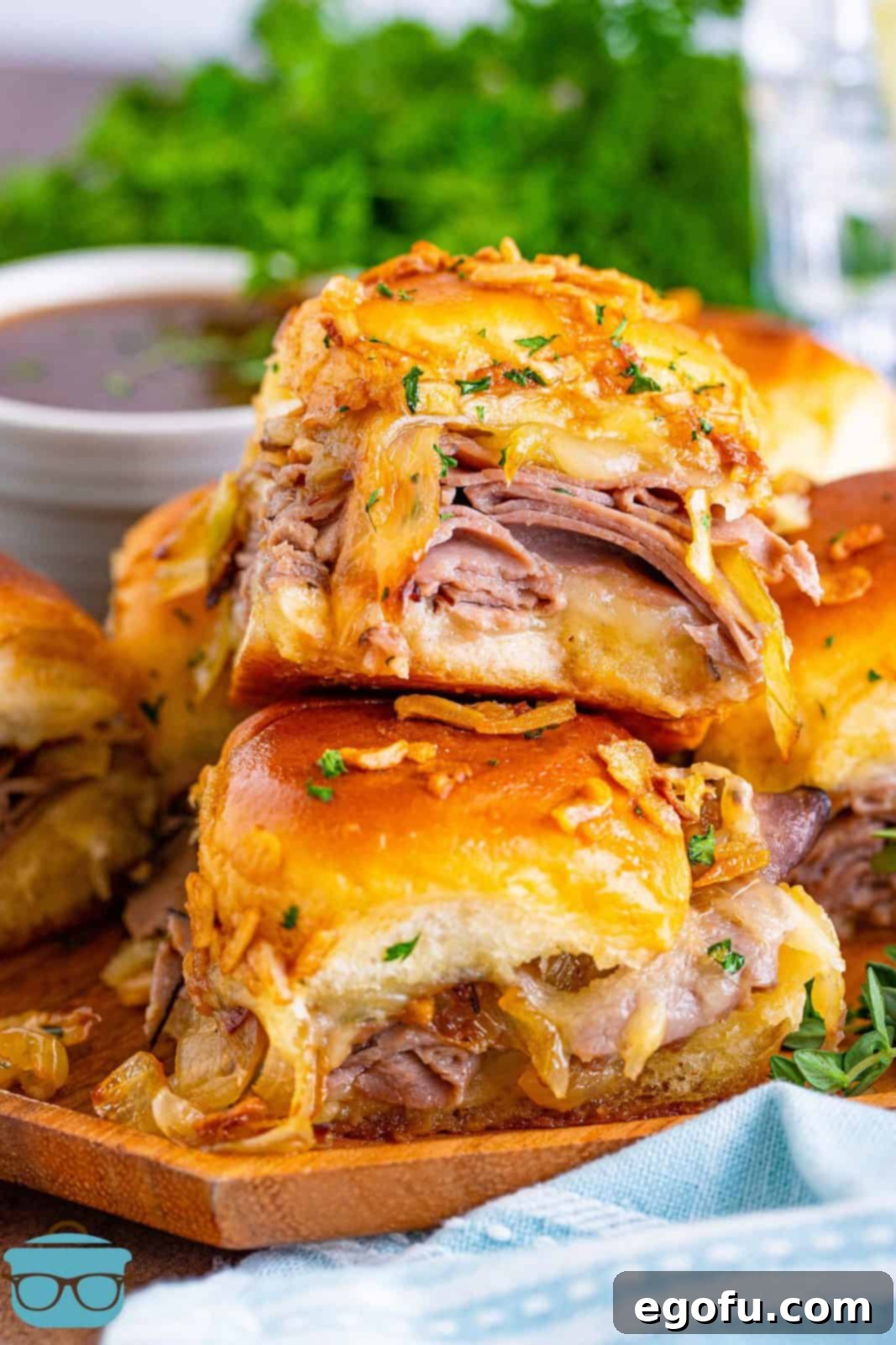 Close up of stacked French Dip Sliders on plate with melted cheese and onions.