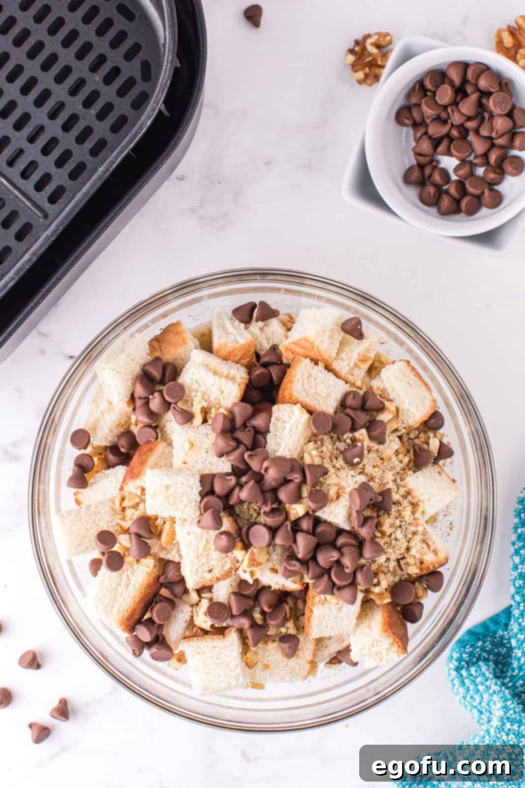 Chocolate chips and chopped walnuts added to cubed bread in a bowl, ready for the liquid mixture.
