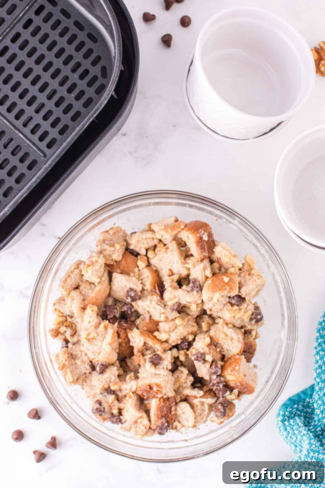 Liquid custard mixture poured over bread cubes, walnuts, and chocolate chips, being stirred to ensure even saturation.
