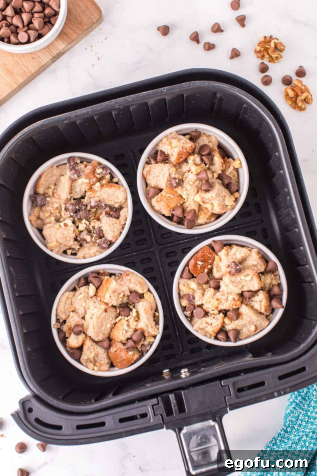 Bread mixture carefully portioned into individual ramekins and placed in the basket of an air fryer, ready for cooking.
