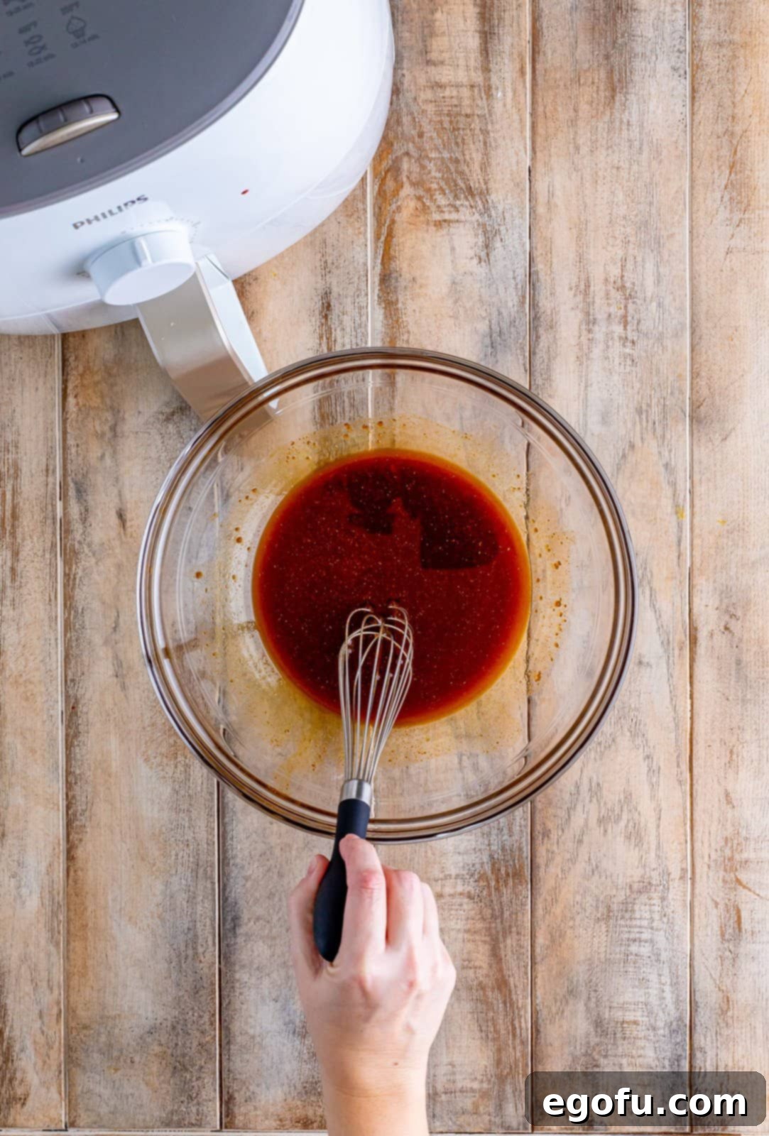 Nashville hot sauce ingredients being whisked together in a clear bowl near the air fryer, preparing to coat the cooked chicken.