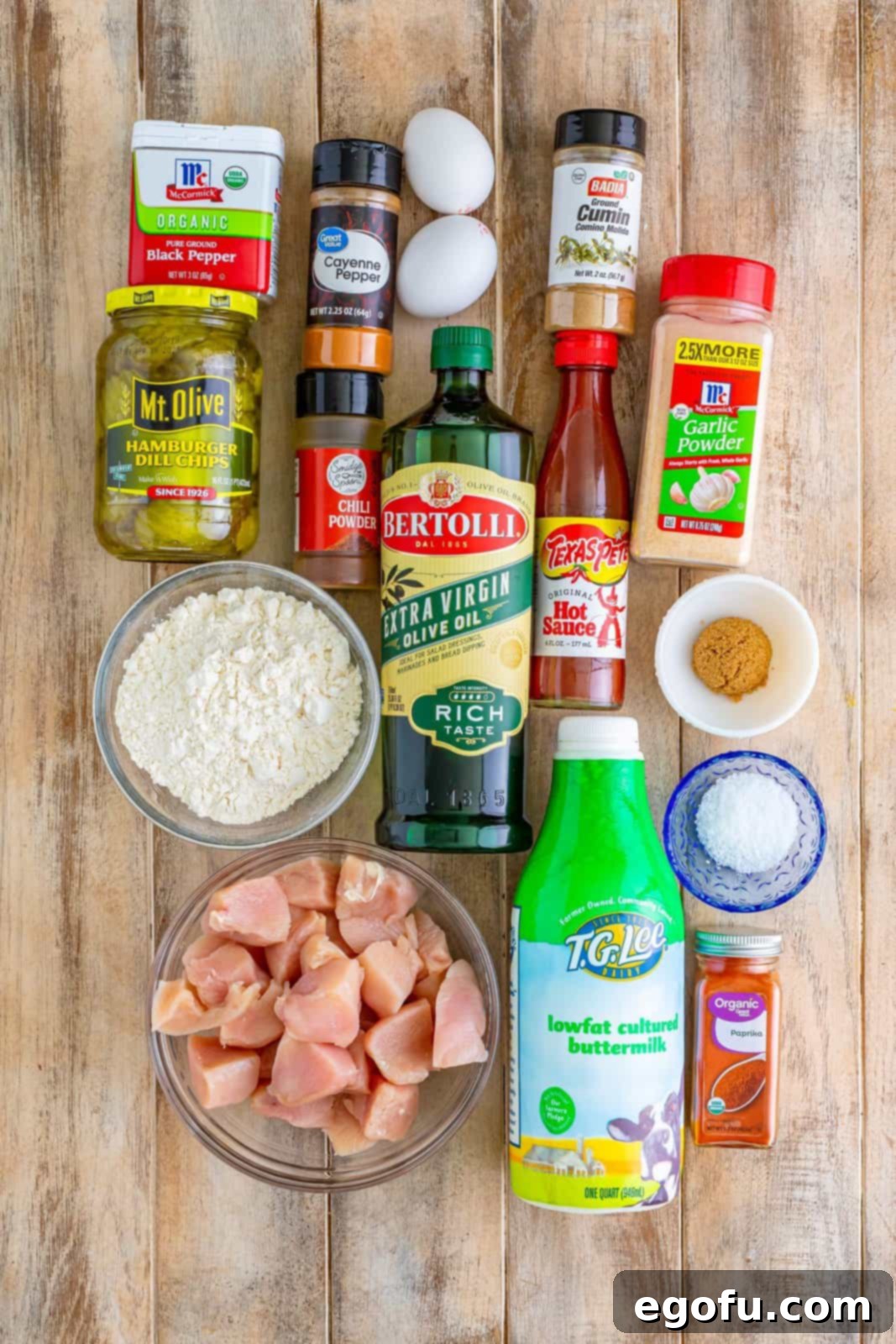 All the fresh ingredients laid out for making Air Fryer Nashville Hot Chicken Nuggets: chicken breasts, eggs, dill pickles, all-purpose flour, kosher salt, chili powder, garlic powder, paprika, cumin, pepper, pickle juice, buttermilk, hot sauce, cayenne pepper, dark brown sugar, and olive oil.