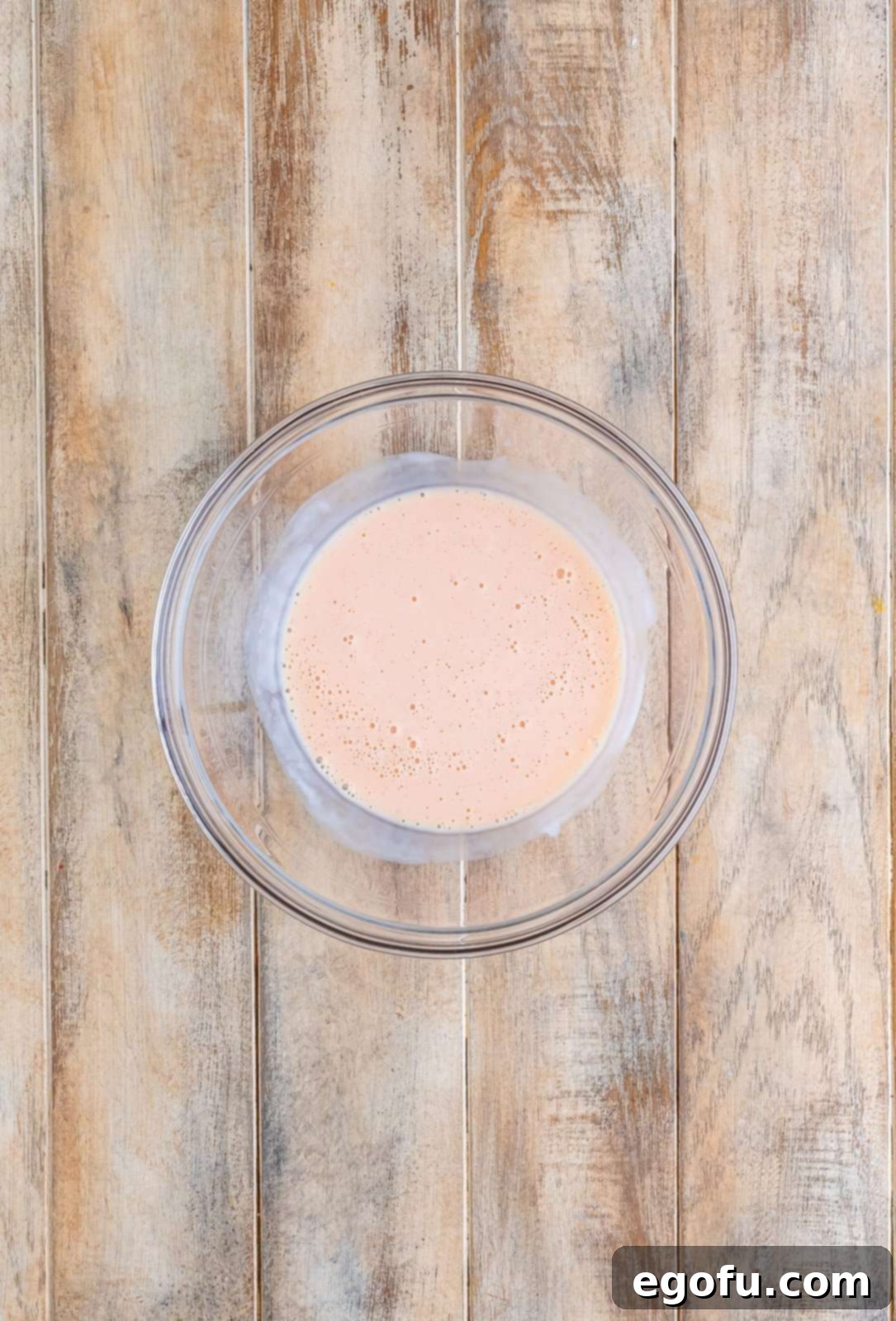 Buttermilk, pickle juice, and hot sauce being whisked together in a clear bowl to create the brine mixture.