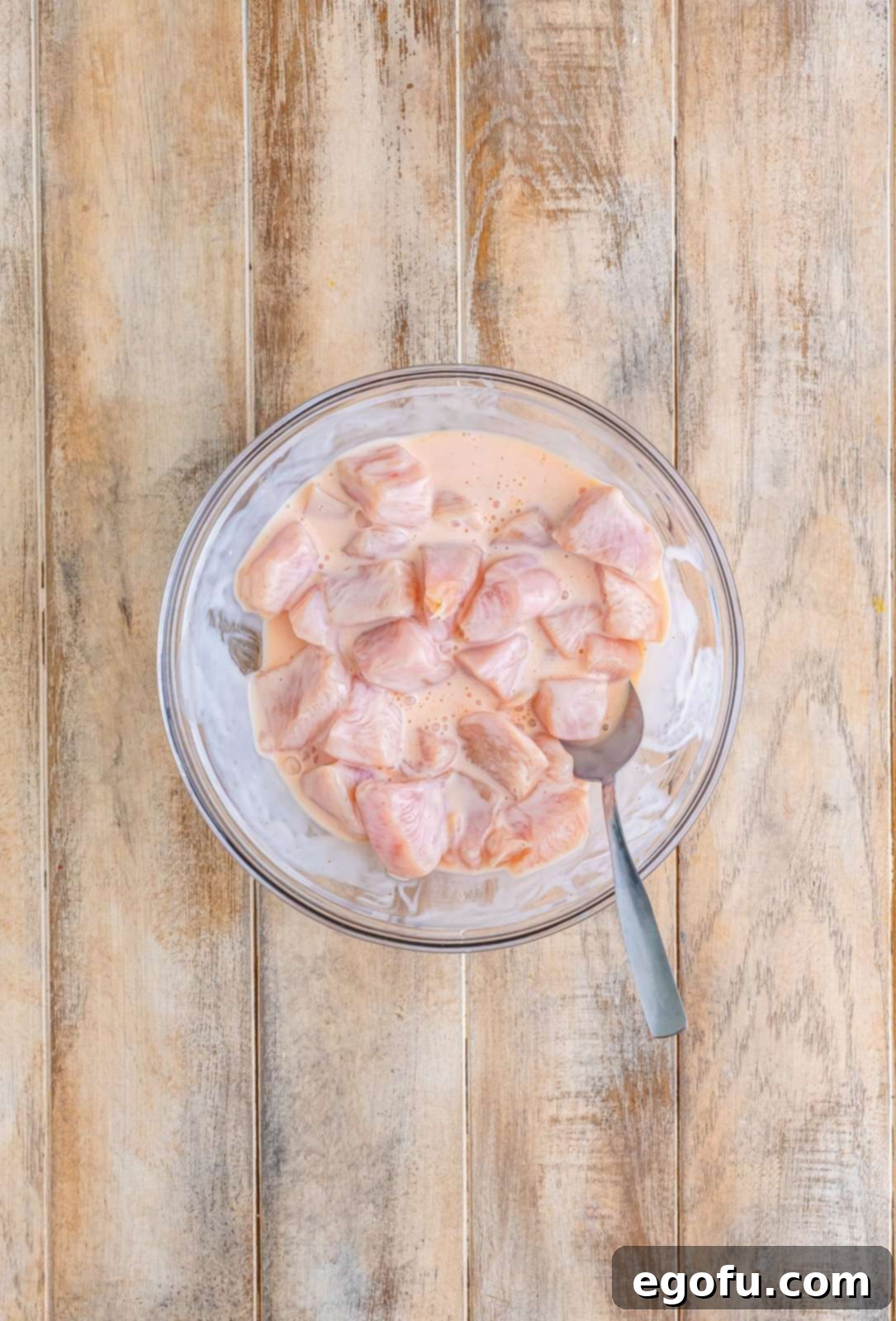 Diced chicken meat soaking in the buttermilk brine in a clear bowl, ready for flavor infusion.