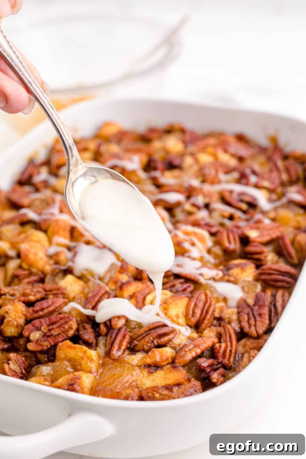 Gooey Cinnamon Roll Delight 12 Spoon drizzling icing over finished casserole.