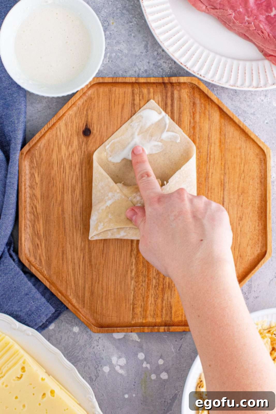 A finger applying the flour and water paste to the top corner of the egg roll wrapper to seal it securely.