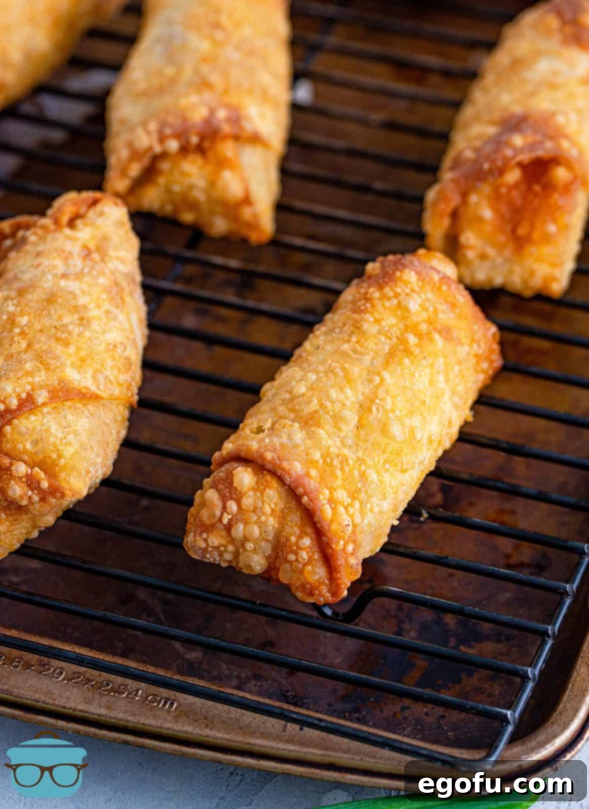 Golden-brown Reuben Egg Rolls resting on a wire rack over a baking sheet, allowing excess oil to drip off for a perfectly crisp finish.