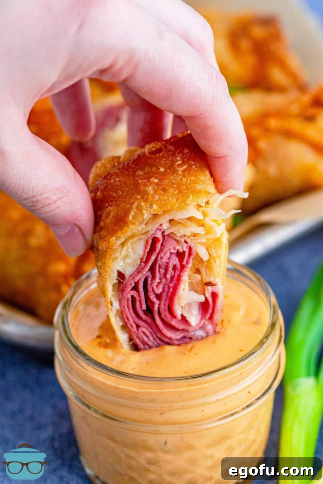 A freshly cut Reuben Egg Roll, revealing its savory filling, being dipped into a creamy pool of Thousand Island dressing, ready to be enjoyed.