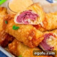 Square image of Reuben Egg Rolls stacked on tray with top one cut in half showing inside.