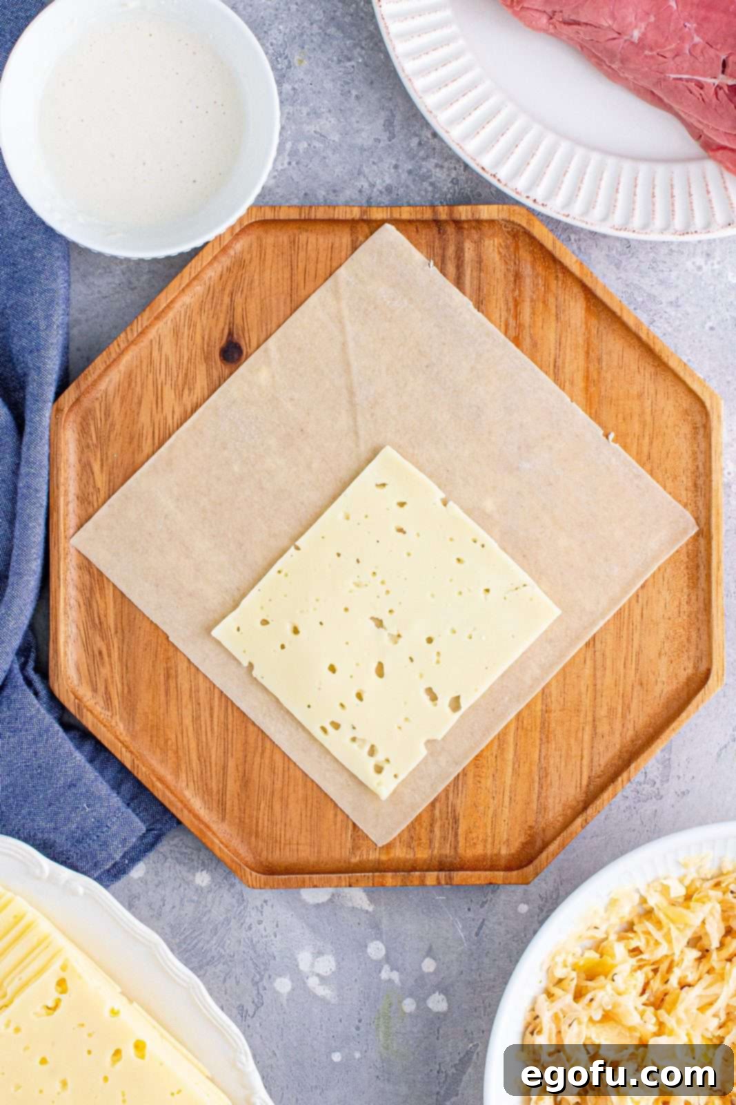 A single slice of Swiss cheese meticulously placed on the bottom corner of an egg roll wrapper, ready for additional fillings.