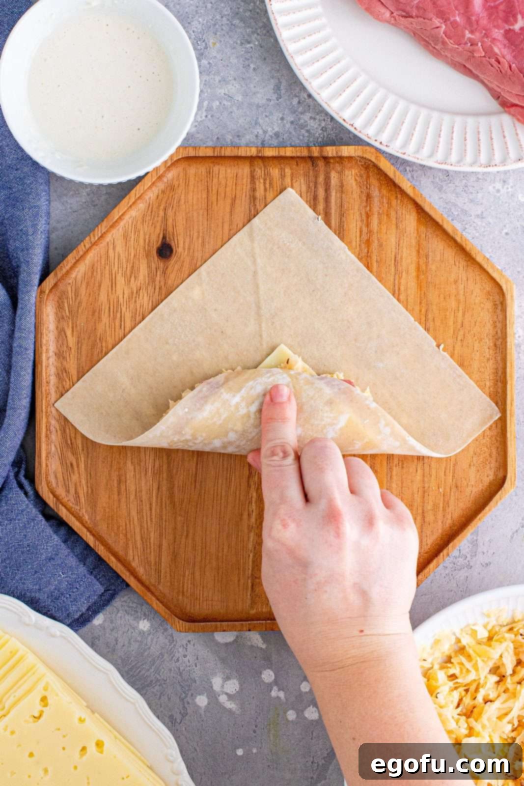 The bottom corner of the egg roll wrapper neatly folded up and over the filling, initiating the rolling process.
