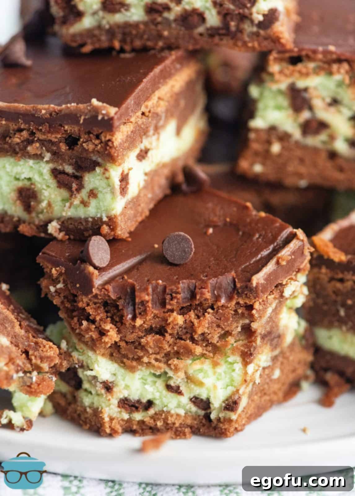 Close up of stacked Mint Cream Cheese Brownies on white plate, highlighting the creamy green mint layer.