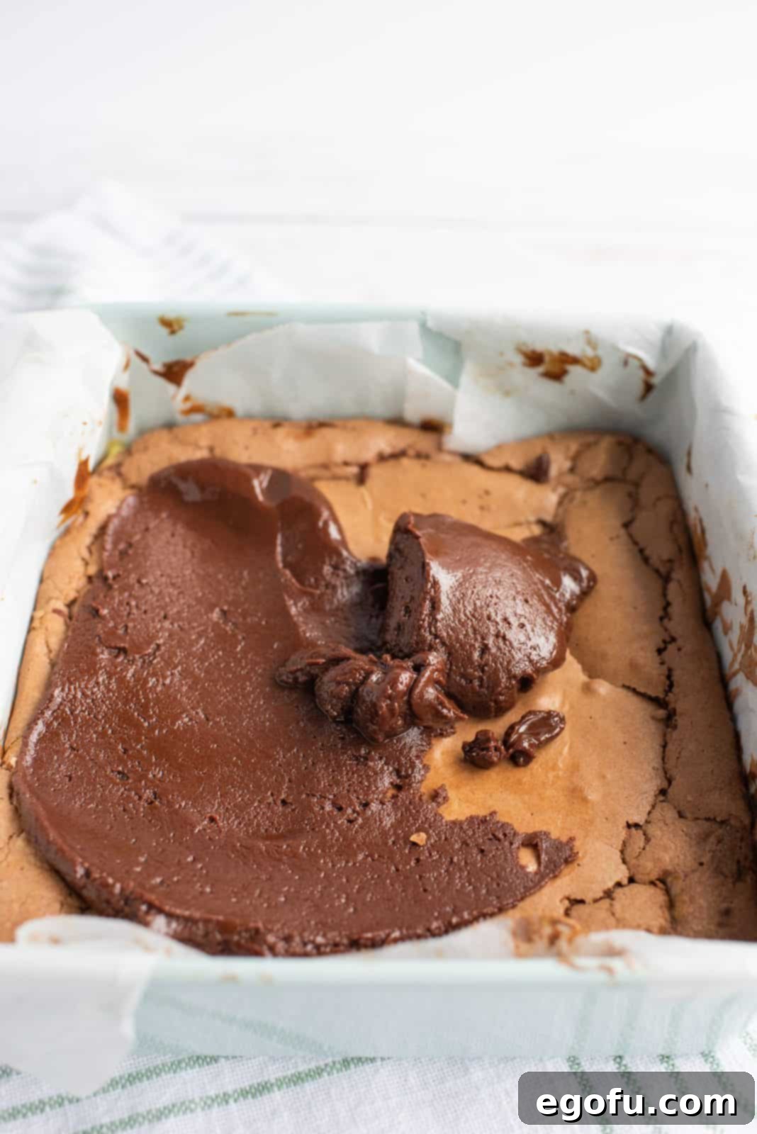 Chocolate frosting being spread smoothly over the cooled Mint Cream Cheese Brownies.